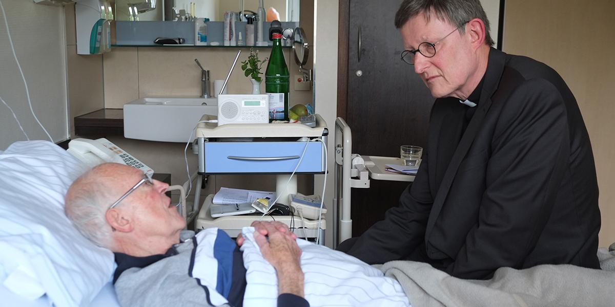 Der Kölner Erzbischof Rainer Maria Kardinal Woelki sitzt am Bett eines Patienten im Marien Hospital Düsseldorf.
