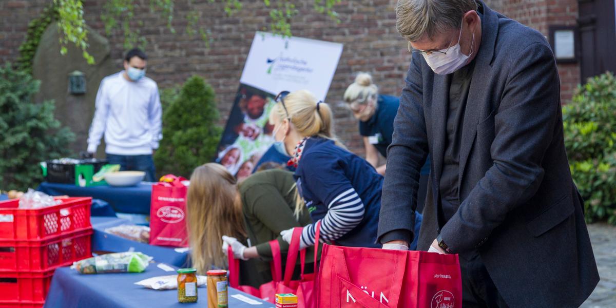 Kardinal Woelki packt mit Mitarbeitenden der KJA Köln Lebensmitteltaschen für bedürftige Kinder und Familien