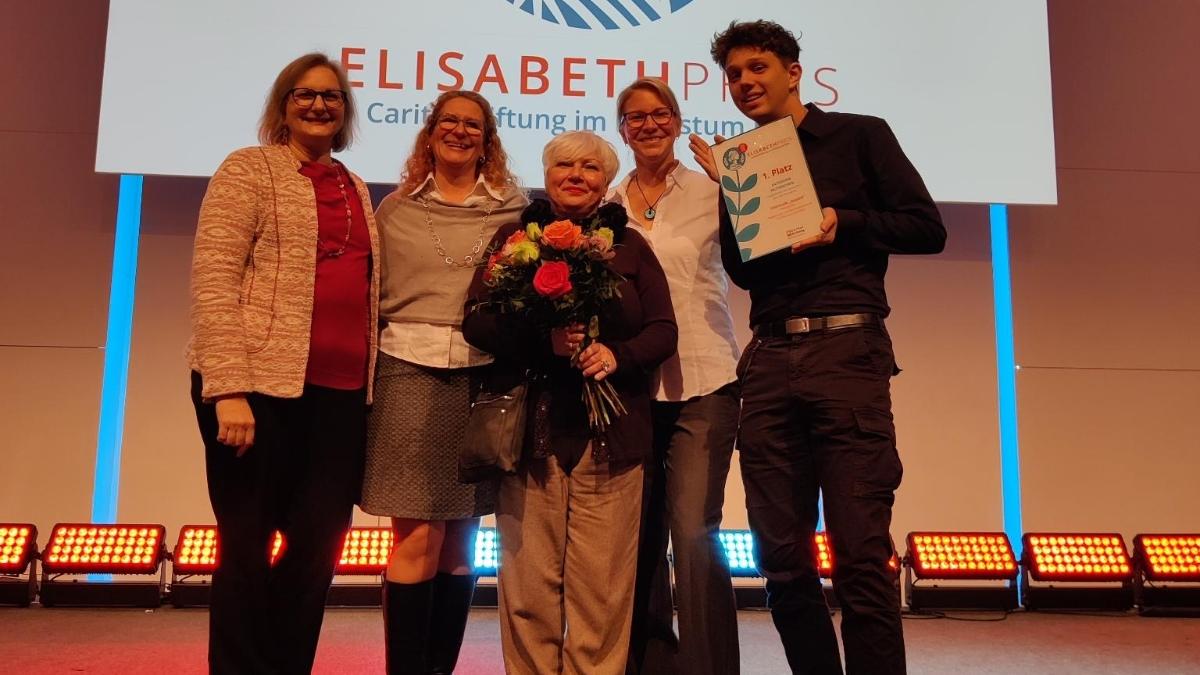 Ein Foto zeigt fünf Personen auf einer Bühne. Im Hintergrund ist das Logo des Elisabeth Preis zu sehen.