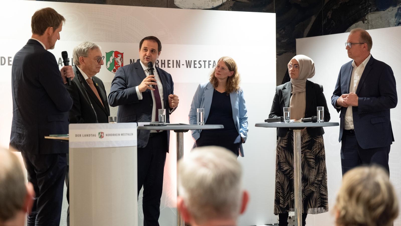 Ein Foto zeigt sechs Personen im Gespräch auf einer Bühne.