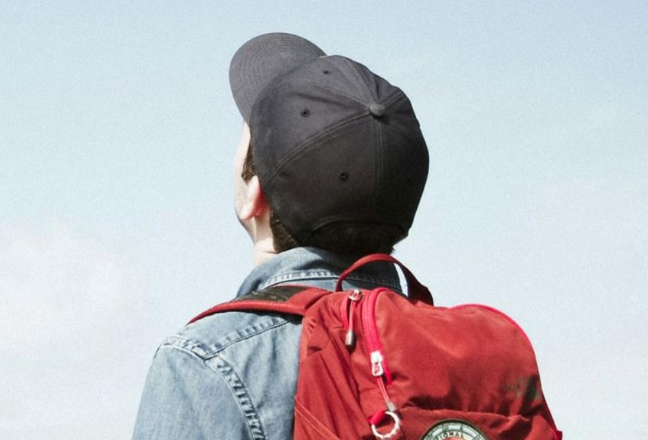 Kind mit Rucksack und Baseballcap schaut in den hellblauen Himmel