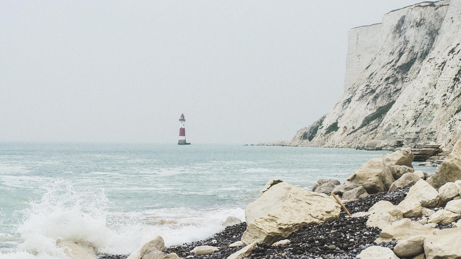 Leuchtturm im Meer an einer schroffen Küstenlandschaft