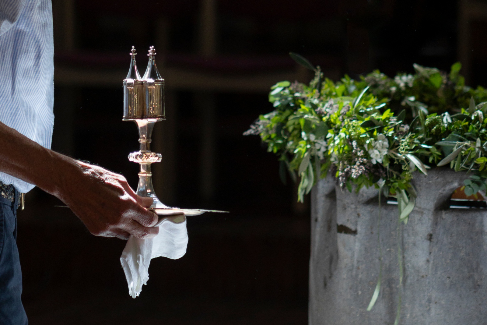 Silbernes Ölgefäß, dahinter geschmücktes Taufbecken.