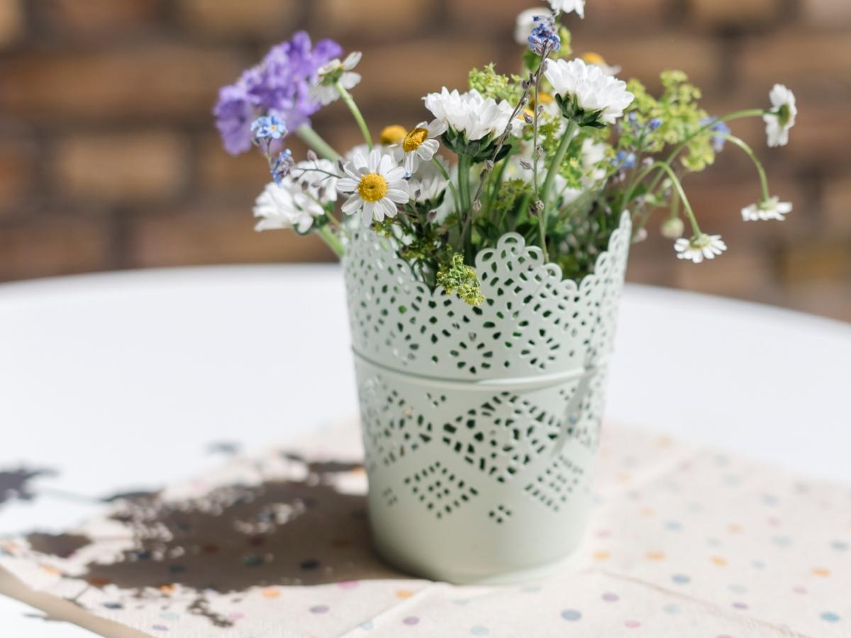 Blumenvase auf weiß gedecktem Tisch vor Steinwand.