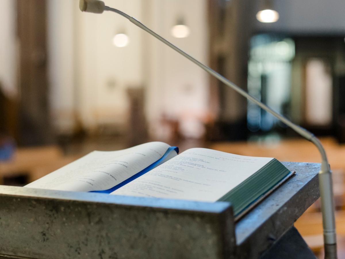 Bibel auf Lesepult, im Hintergrund Kirche.