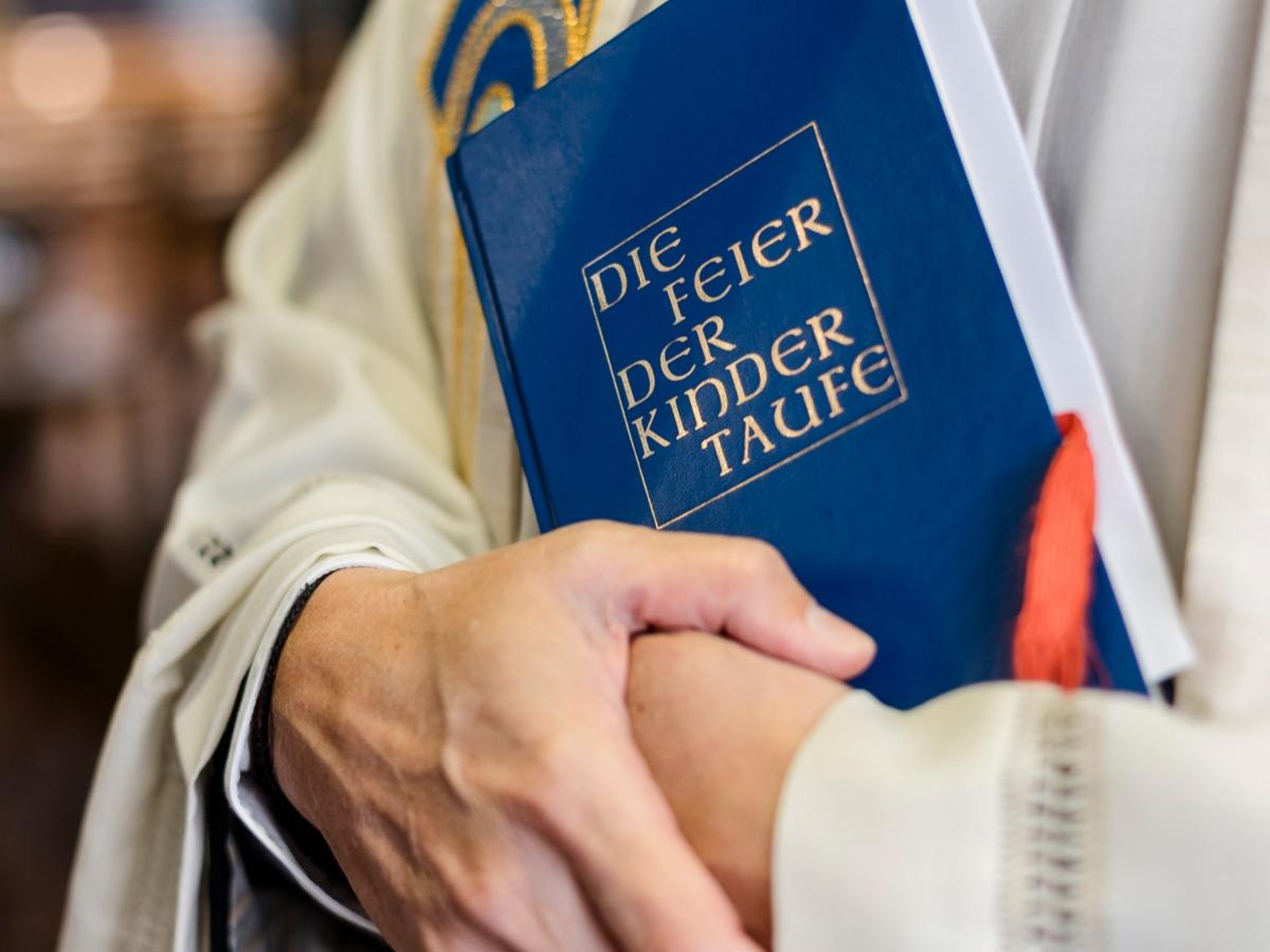 Priester hält Buch für Kindertaufe.