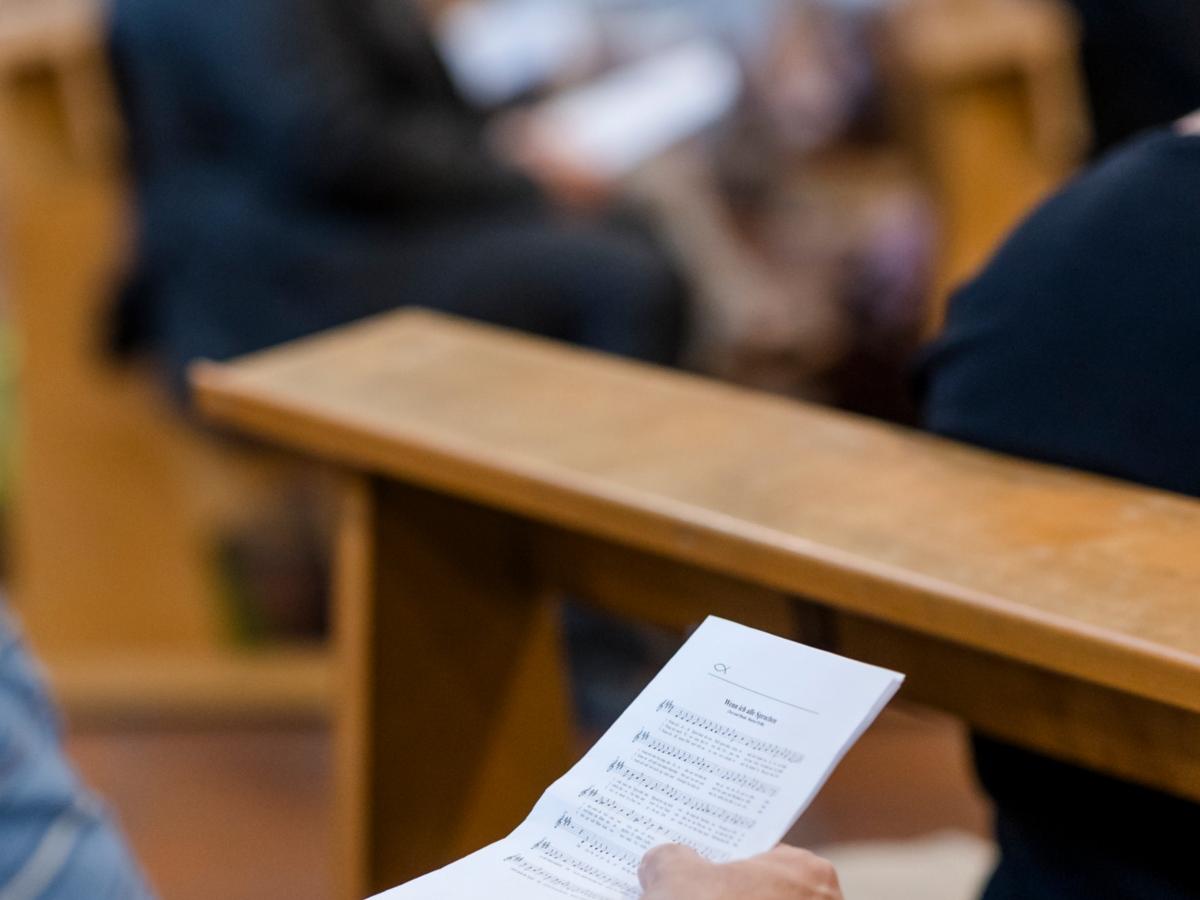 Person hält Liedzettel, Menschen in Bänken.