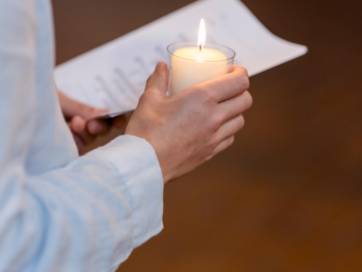 Person hält Kerze und Liedblatt.