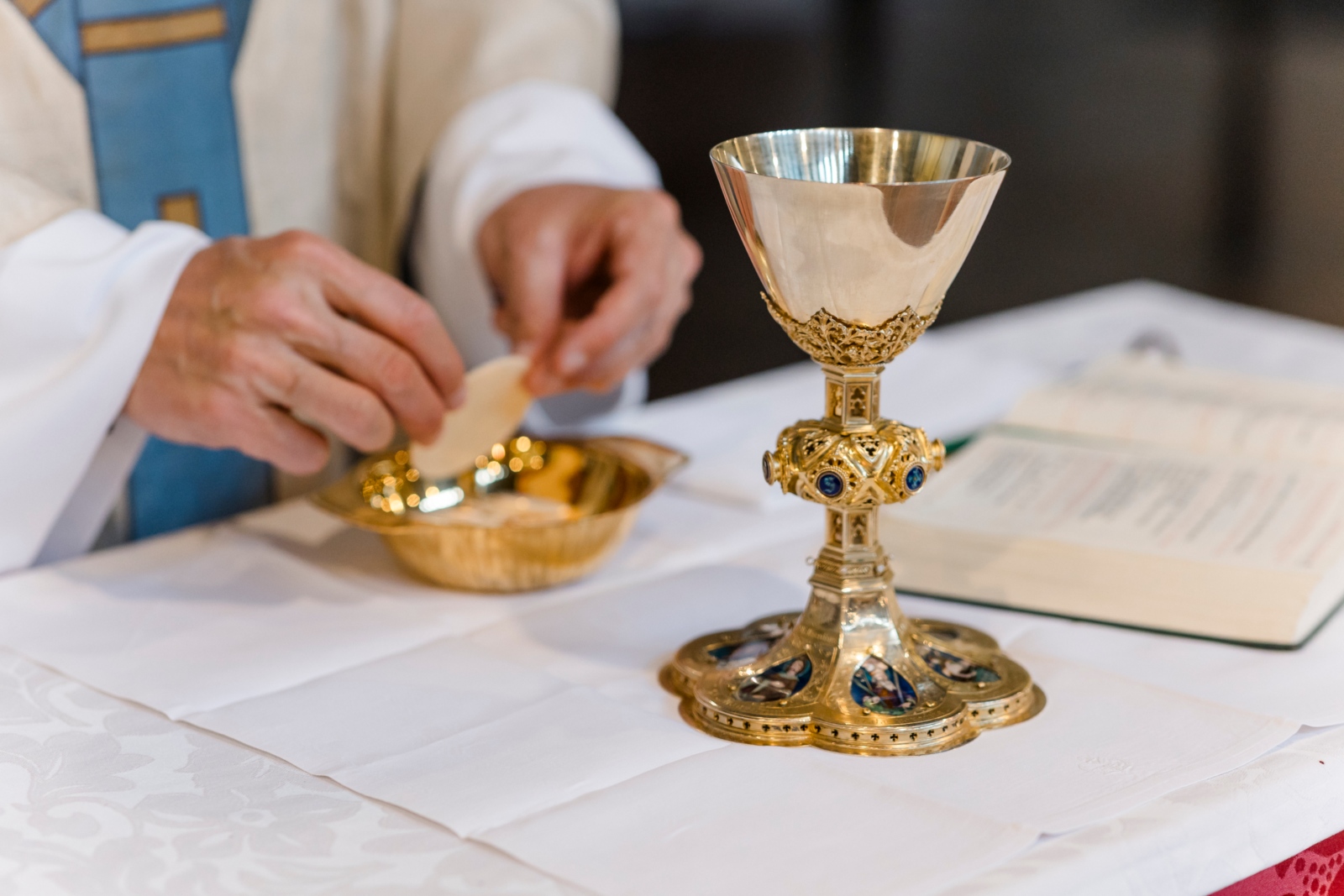 Priester bricht Hostie über Schale.